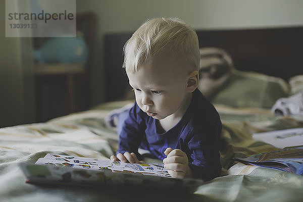 Junge schaut sich ein Buch an  während er im Schlafzimmer auf dem Bett liegt