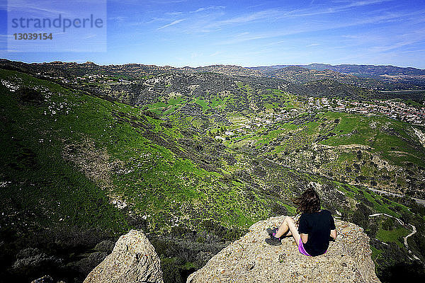 Hochwinkelansicht einer Frau  die auf einer Klippe vor der Landschaft sitzt