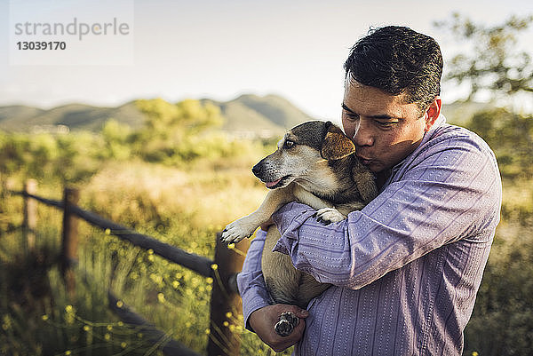 Mann küsst Hund  während er ihn auf dem Feld umarmt