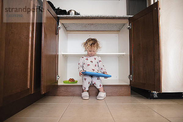Mädchen in voller Länge hält Spielzeug  während es zu Hause im Schrank sitzt