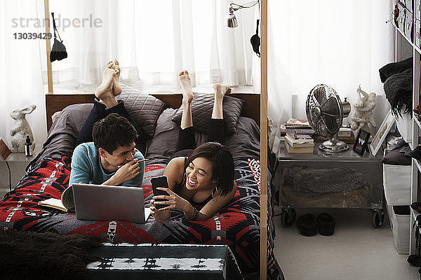 Fröhliches Paar benutzt Laptop  während es zu Hause auf einem Himmelbett liegt