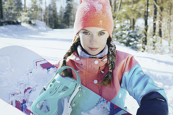 Porträt einer Frau  die im Winter im Wald stehend ein Snowboard hält