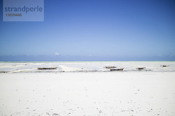 Boote vertäut auf Sand am Strand vor blauem Himmel