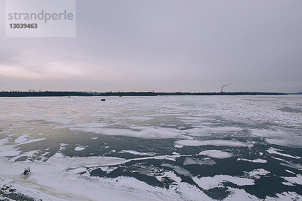 Szenische Ansicht eines zugefrorenen Flusses vor bewölktem Himmel