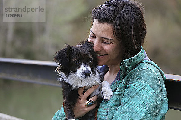 Glückliche Frau umarmt Border Collie  während sie im Park auf einer Bank sitzt