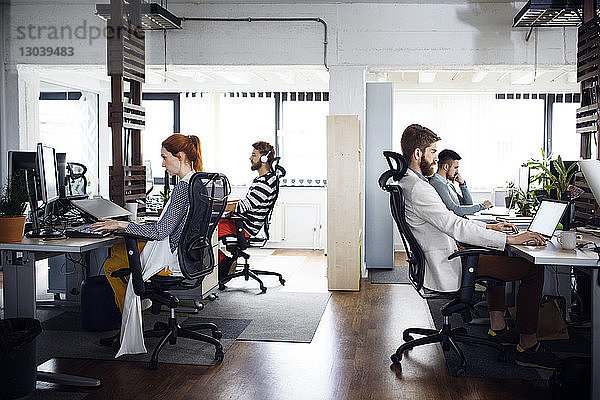 Seitenansicht von Geschäftsleuten  die an Computer-Schreibtischen im Kreativbüro arbeiten