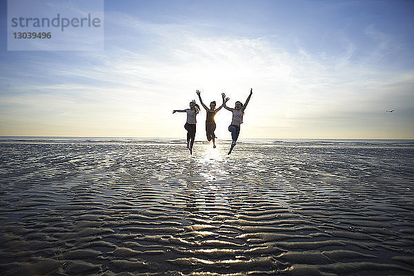 Weibliche Freunde springen am Strand gegen den Himmel
