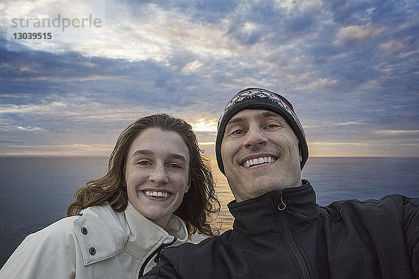 Porträt eines glücklichen Vaters mit Tochter bei Sonnenuntergang am Meer stehend