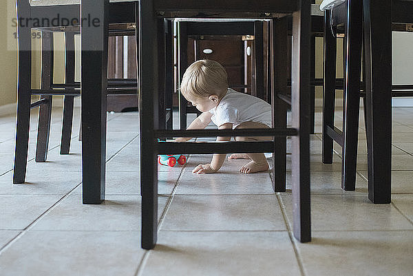 Kleiner Junge spielt zu Hause mit Spielzeug unter dem Esstisch