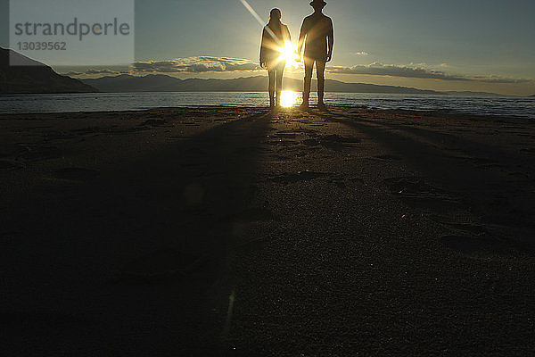 Silhouettenpaar steht bei Sonnenuntergang auf Sand am See