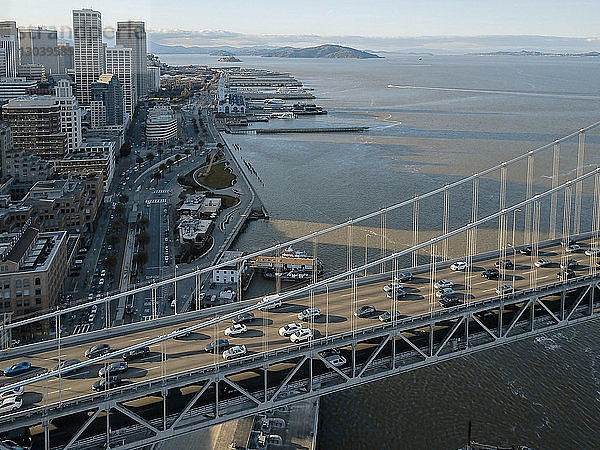 Hochwinkelaufnahme von Autos  die sich bei Sonnenuntergang auf der Oakland Bay Bridge über das Meer in der Stadt bewegen