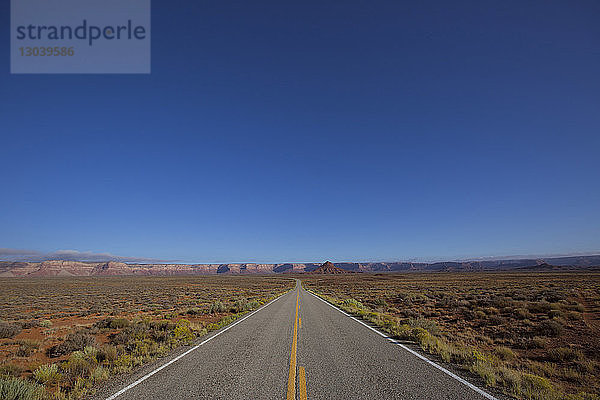 Leere Straße inmitten der Landschaft bei strahlend blauem Himmel am sonnigen Tag