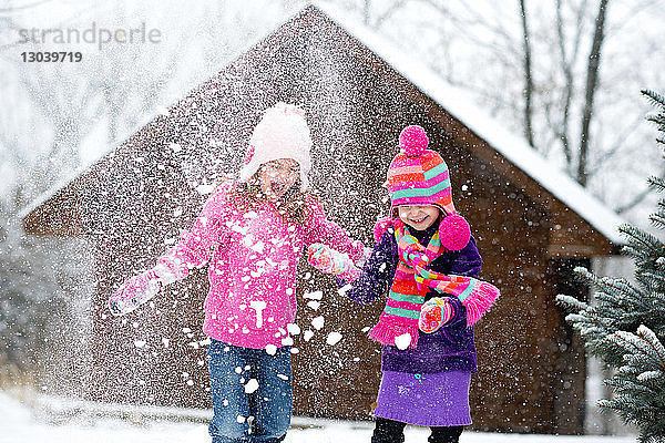 Glückliche Schwestern spielen bei Schneefall mit Schnee