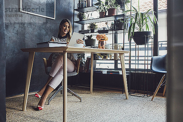 Lächelnde Geschäftsfrau  die am Tablet-Computer arbeitet  während sie im Home-Office am Tisch sitzt