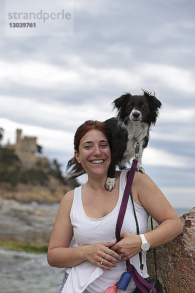 Porträt einer glücklichen Frau mit Hund auf der Schulter am Strand