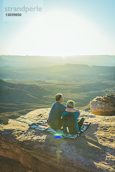 Rückansicht eines Paares  das an einem sonnigen Tag im Canyonlands-Nationalpark auf einem Berg sitzt