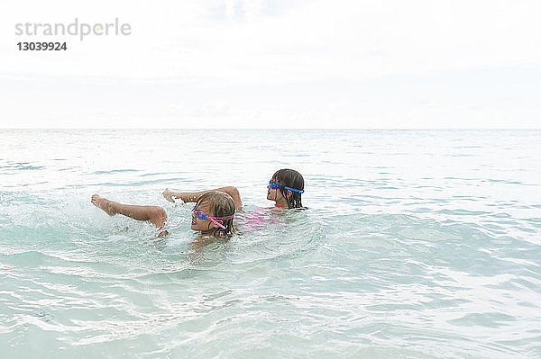 Glückliche Schwestern schwimmen im Meer gegen den Himmel