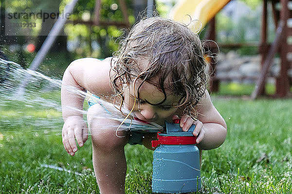 Verspieltes Mädchen trinkt Wasser aus Sprinkleranlage im Hof