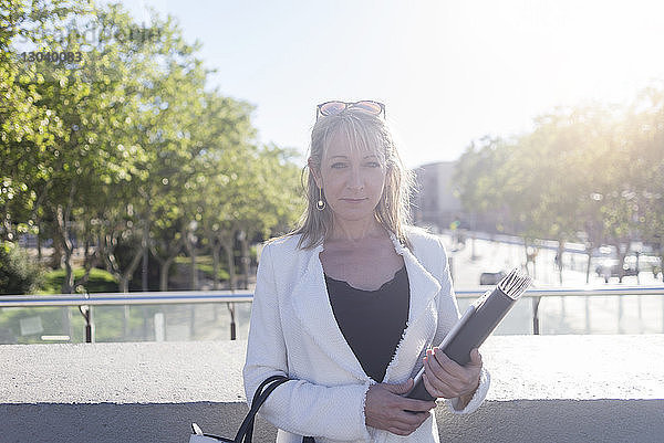 Porträt einer selbstbewussten Geschäftsfrau  die eine Akte hält  während sie bei strahlendem Sonnenschein in der Stadt steht