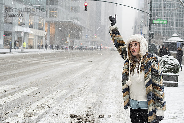 Frau ruft Taxi  während sie auf schneebedeckter Straße in der Stadt steht