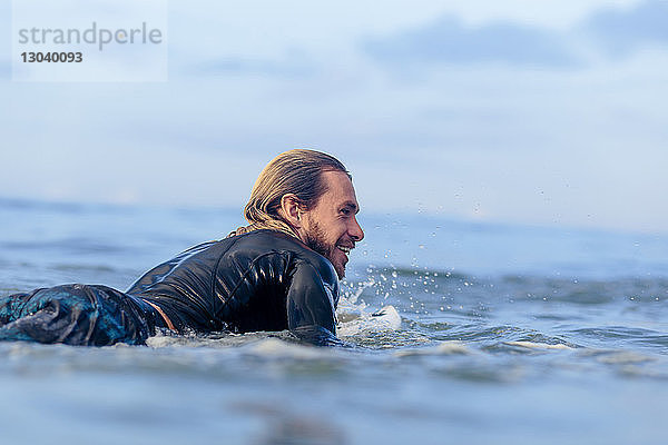 Glücklicher Mann liegt auf einem Surfbrett im Meer gegen den Himmel