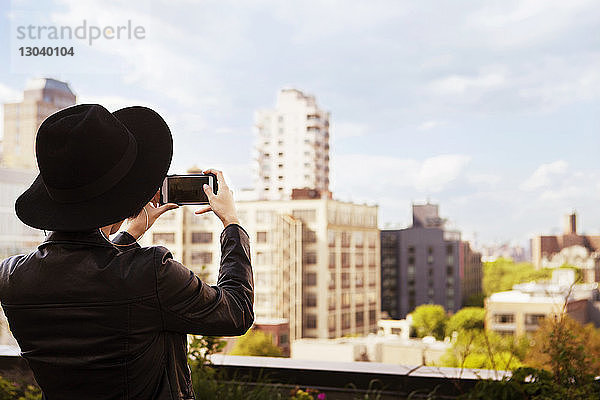 Rückansicht einer Frau  die Gebäude mit einem Smartphone von der Terrasse aus fotografiert