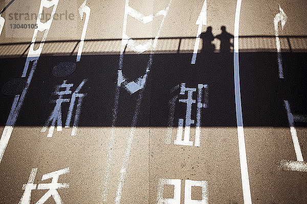 Hochwinkelansicht eines japanischen Textes auf der Straße mit Schatten von Personen auf der Brücke