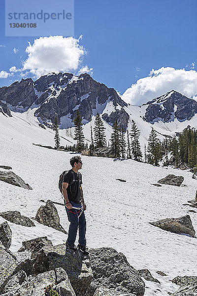 Mann in voller Länge auf Felsen am schneebedeckten Berg gegen den Himmel stehend