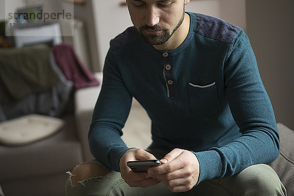 Mann benutzt Mobiltelefon  während er zu Hause auf dem Sofa sitzt