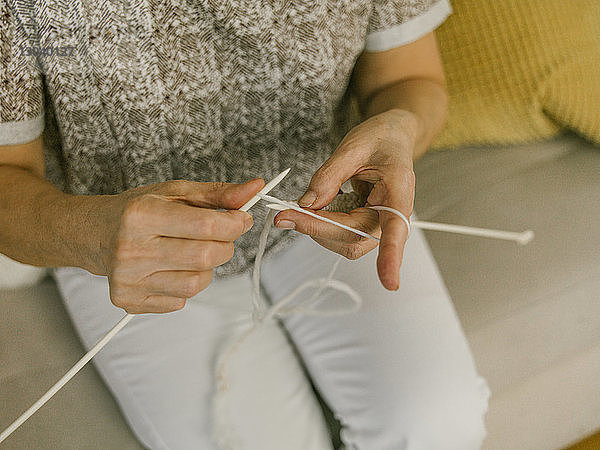 Hochwinkelansicht einer Frau  die strickt  während sie zu Hause auf dem Sofa sitzt