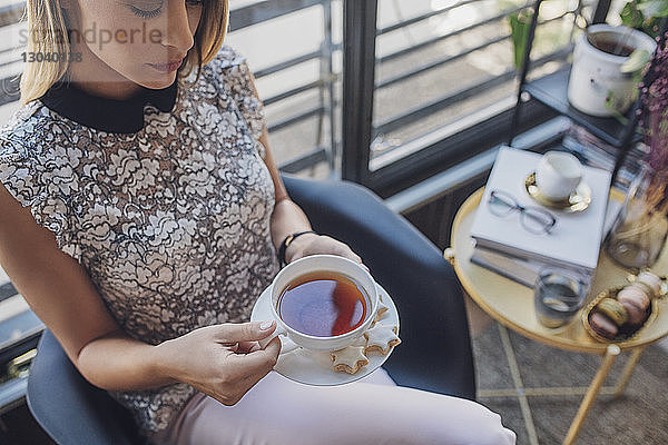 Schrägansicht einer Geschäftsfrau  die eine Kaffeetasse hält  während sie im Heimbüro auf einem Stuhl sitzt