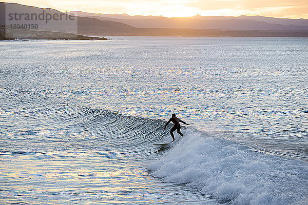 Mann surft bei Sonnenuntergang im Meer