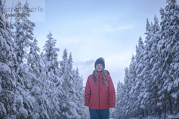 Frau schaut weg  während sie im Winter inmitten von Bäumen steht