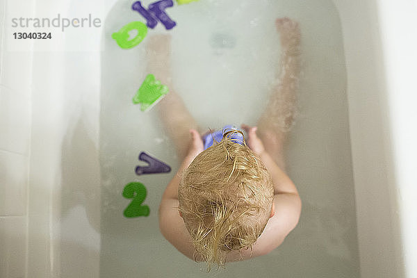 Draufsicht auf einen nackten Jungen  der zu Hause in der Badewanne mit Spielzeug spielt