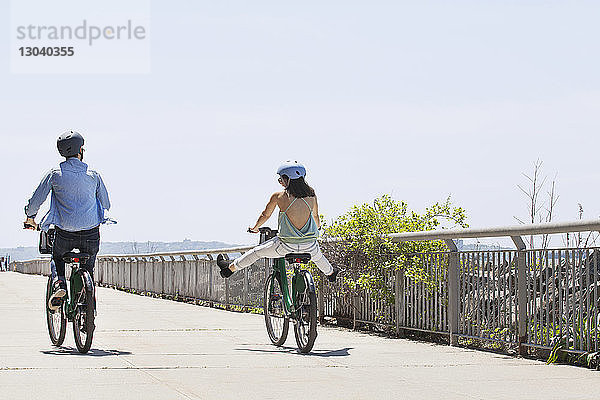 Rückansicht eines Fahrrad fahrenden Paares auf der Promenade bei klarem Himmel
