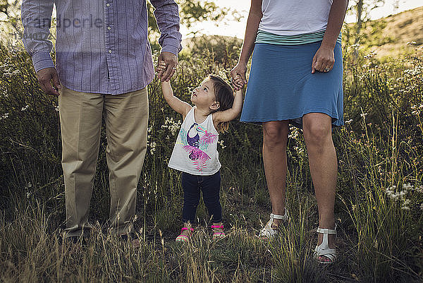 Niedriger Teil der Eltern hält die Tochter an der Hand  während sie auf einem Grasfeld stehen