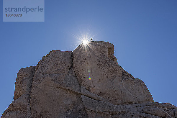 Tiefwinkelansicht eines auf einem Felsen stehenden Mannes vor klarem blauen Himmel