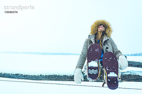 Fröhliche Frau sitzt auf dem Geländer eines schneebedeckten Feldes