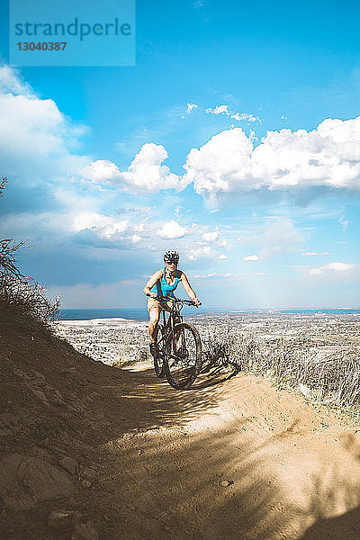 Mountainbike fahrende Radfahrerin in trockener Landschaft vor bewölktem Himmel