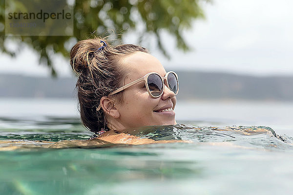 Lächelnde Frau mit Sonnenbrille schwimmt im Meer