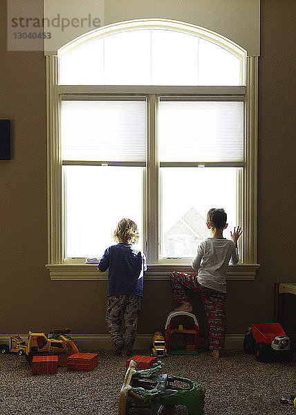 Rückansicht von Jungen  die zu Hause durch das Fenster schauen