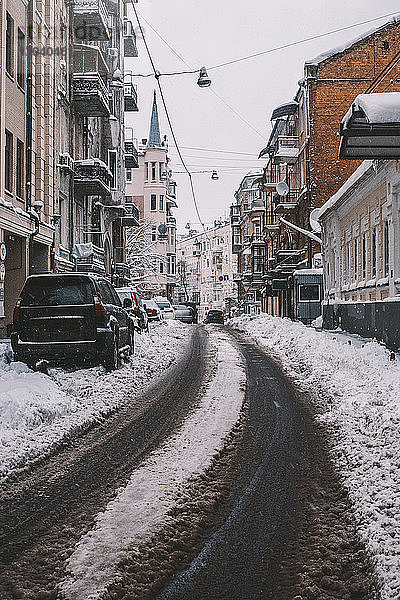 Autos parken auf schneebedeckter Straße inmitten von Gebäuden in der Stadt