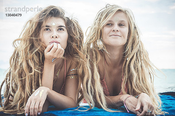 Freundinnen mit Dreadlocks  die sich am Strand gegen den Himmel entspannen