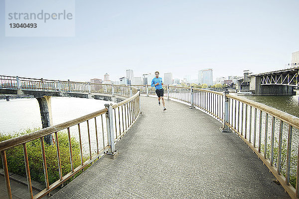 Junger Mann joggt auf Brücke bei klarem Himmel