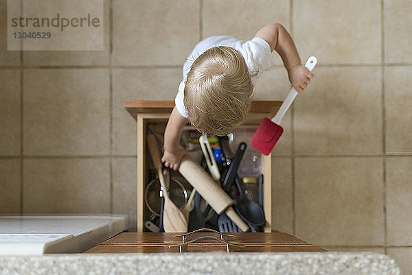 Draufsicht eines kleinen Jungen  der Küchenutensilien aus der Schublade nimmt