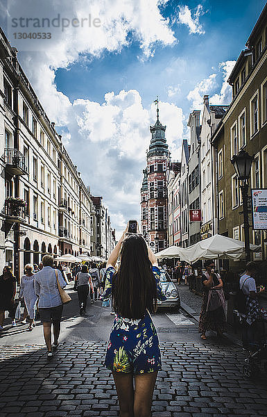 Rückansicht einer Frau  die mit einem Smartphone Gebäude fotografiert  während sie auf dem Markt steht