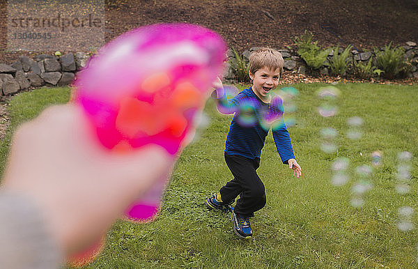 Ausgeschnittenes Bild einer Hand  die eine Blasenpistole hält  während sie mit einem Jungen im Hof spielt