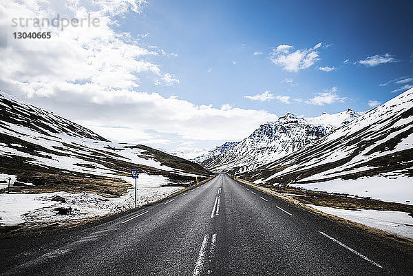Leere Landstraße durch schneebedeckte Berge gegen den Himmel im Winter