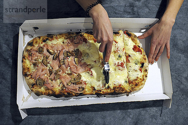 Abgehackte Hände einer Frau  die zu Hause auf der Küchentheke Pizza schneidet