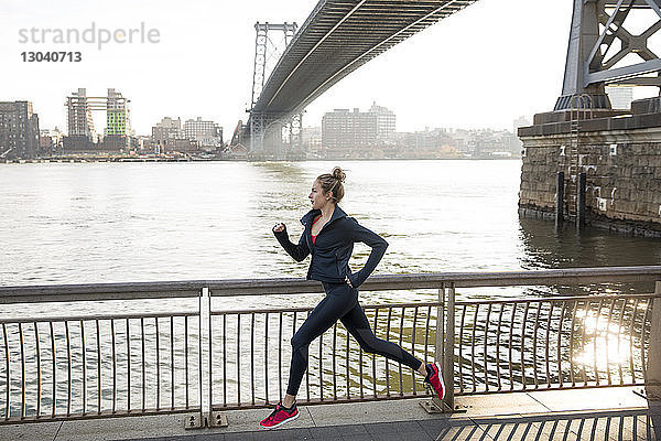 Seitenansicht eines selbstbewussten Athleten beim Laufen auf der Promenade am East River